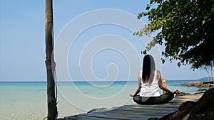 4K. back side of Asian woman practicing concentration with meditation sitting on wooden bridge over the sea during summer vacation