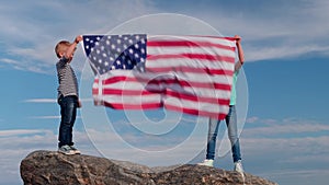 4k. Blonde boy and girl waving national USA flag outdoors over blue sky at summer - american flag, country, patriotism