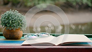 4K. cinemagraph of blank book with flowerpot on the wooden table against the sparkling river background