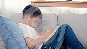 4K, Close Up An Asian boy is dying on the sofa in the living room of the house holding a notepad and is happily drawing on the