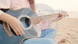 4K. close up of long hair woman playing acoustic guitar at the beach with gentle wind during sunset time, feeling relax