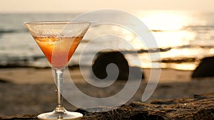 4K. cocktail glass with water droplets on the beach with golden wave reflection during the sunset time