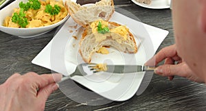 4K: Cut open croissant and some scrambled eggs lie on an angular white plate. A woman is putting some fresh scrambled eggs to the