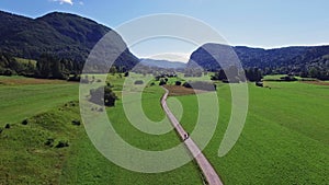 4K. Flight above green Bohinj Lake valley in the morning. People riding bicycles on a path. Stara Fuzina village in Julian Alps.