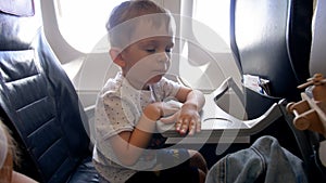 4k footage of adorable 2 years old toddler boy sitting in passenger seat at airplane and playing with folding table