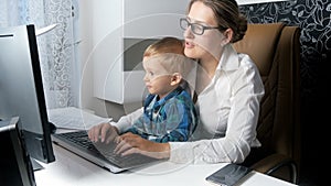 4k footage of beautiful elegant businesswoman working on computer with her adorable toddler son at office