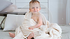 4K footage of cute smiling baby boy covered in towel sitting on bed after bathing