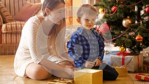 4k footage of happy smiling little boy sitting under Christmas tree and opening his Christmas gifts and presents from