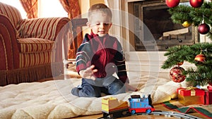 4k footage of little toddler boy looking at toy train riding on circle railroad at living room. Child receiving gifts