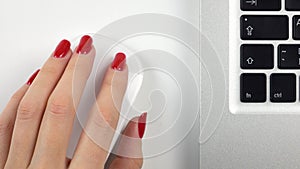 4K footage. Woman`s left hand with red manicure using a wireless computer mouse. Top view. Close-up