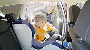 4k footage of young caring mother seating her toddler son in child safety car seat before riding vehicle