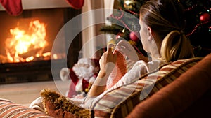 4k footage of young woman knitting wool scarf at burning fireplace and Christmas tree