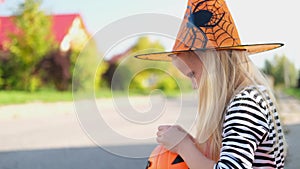 4k. Halloween kids. blonde girl in witch costume and pumpkin bucket. Child eating candy from buckets sitting on street