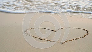 4K. heart drawing on sand beach with soft wave of the blue sea, ripple ocean wave with white bubble foam