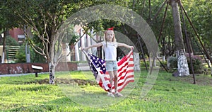 4k. Kid waving national USA flag outdoors. Cute Little Girl seven years old with blonde hair in casual clothing running