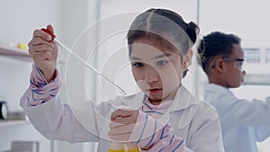 4K, little Asian girl paying attention to science lab jug with yellow liquid inside, learns with friends in  white science