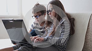 4k. little cute caucasian girl and boy in glasses study in laptop