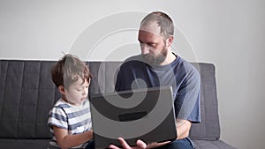 4k. little son learning online with father on the couch. Laptop.