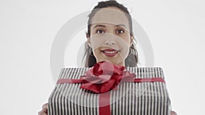 4K portrait of appealing young smiling woman with brown eyes looking at camera and presenting to viewer gift wrapped in