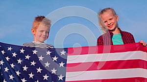 4k. Portrait of blonde boy and girl with national USA flag outdoors over blue sky on sunset at summer - american flag