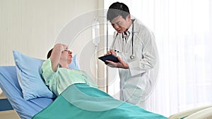 4K Senior doctor talks to caucasian patient on bedside in the hospital as he holds a tablet computer