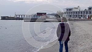 4K Shot from back. The woman appears from behind the camera and walks along the spring beach