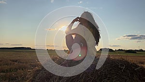 4k Silhouette of dreaming woman in a dress sitting on a haystack against sun.