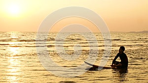 4K. silhouette of surfer man relax by sitting on surfboard over the sea at sunset on tropical beach. sport and recreation