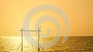 4K. silhouette of two swing swaying over the sea during sunset time with yellow golden sky reflect on the ocean surface.