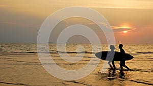 4K. silhouette of young happy surf man and woman running with long surf boards at sunset on tropical beach. surfer on the beach