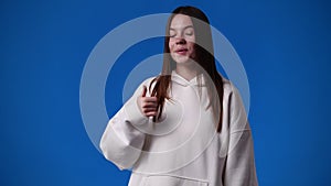 4k slow motion video of cute girl pointing at left and showing thumb up over blue background.