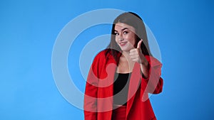 4k slow motion video of one girl pointing at left and showing thumbs up on blue background.