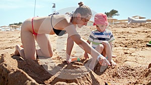 4k slow motion video of young mother playing with her toddler son while relaxing on sandy sea beach