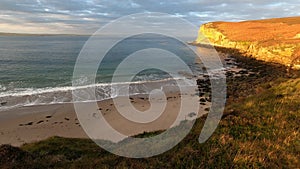 4k time lapse footage of waves breaking on Peddie Sands beach in Caithness, Scotland with sunlight moving on cliffs