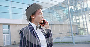 4k. Travel, digtal, business. Attractive African American woman in stylish stripped suit talks on the phone walking