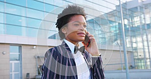 4k. Travel, digtal, business. Attractive African American woman in stylish stripped suit talks on the phone walking