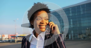 4k. Travel, digtal, business. Attractive African American woman in stylish stripped suit talks on the phone walking