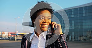 4k. Travel, digtal, business. Attractive African American woman in stylish stripped suit talks on the phone walking