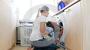 4k video of beautiful young woman taking clean clothes out of washing machine in bathroom