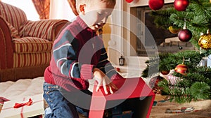 4k video of cheerful smiling little boy taking off the lid from Christmas gift box and taking out toy train that SAnta