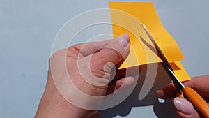 4k video. Close-up of female hands cutting orange paper with small scissors