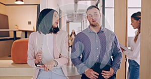 4k video footage of two young business colleagues chatting as they walk though the office