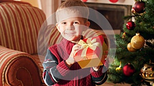 4k video of happy laughing little boy with Christmas gift in beautiful box standing at Christmas tree and looking in