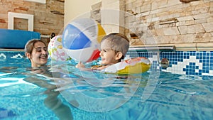 4k video of happy lauhging toddler boy in inflatable ring playing with mother and throwing colorful beach ball at