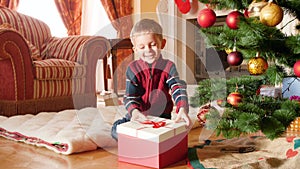 4k video of happy smiling little boy opens his Christmas gift from Santa Claus and taking out toy train. Child receiving