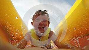 4K Video: Little boy slides fast by the inflatable slide into the water pool with active camera in front of his face