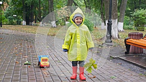 4k video of little boy in yellow plastic raincoat walking in park while raining