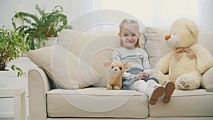 4k video of little curious girl with teddy bear sitting on white couch.