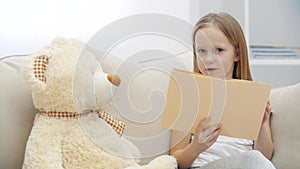 4k video of little girl reading a book to her teddy bear.