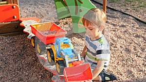 4k video of little toddler boy playing in sandbox and loading gravel and sand in toy trailer with plastic shovel